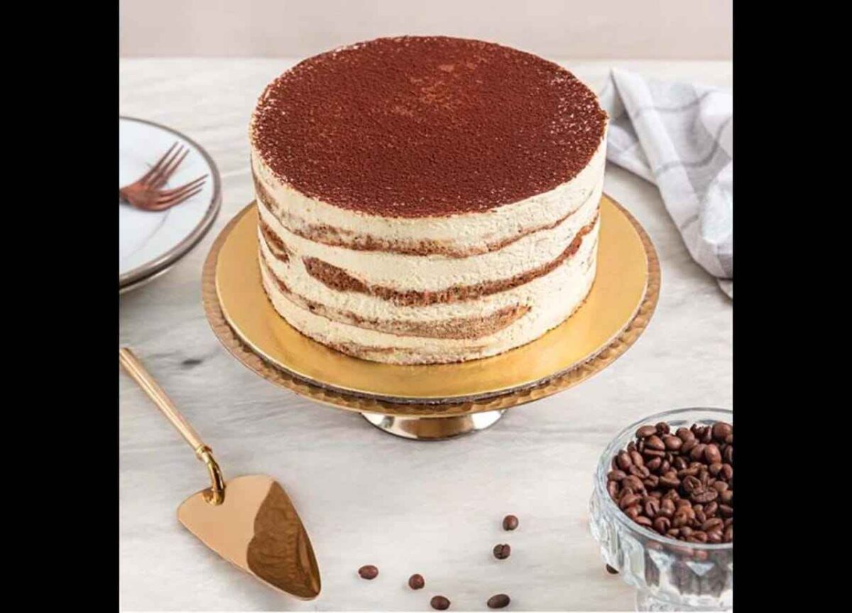 Cream layered cake dusted with cocoa powder on golden cake stand