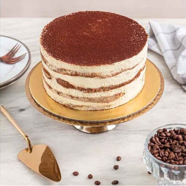 Cream layered cake dusted with cocoa powder on golden cake stand
